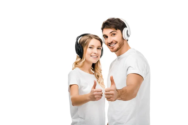 Happy young couple in headphones showing thumbs up and smiling at camera isolated on white — Stock Photo