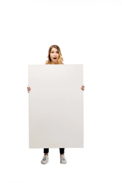 Impactado chica rubia sosteniendo pancarta en blanco y mirando a la cámara aislada en blanco - foto de stock