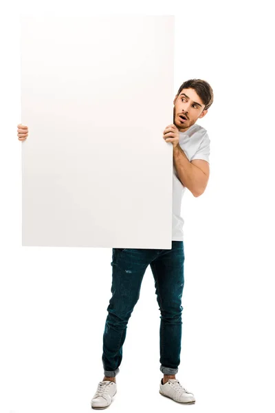 Joven asustado sosteniendo la pancarta en blanco y mirando el espacio de copia aislado en blanco - foto de stock