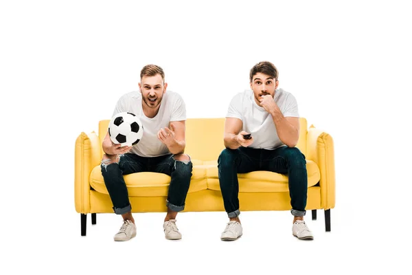 Emotionale junge Männer mit Fußballball sitzen auf der Couch und schauen sich vereinzelt Sportspiele auf weiß an — Stockfoto