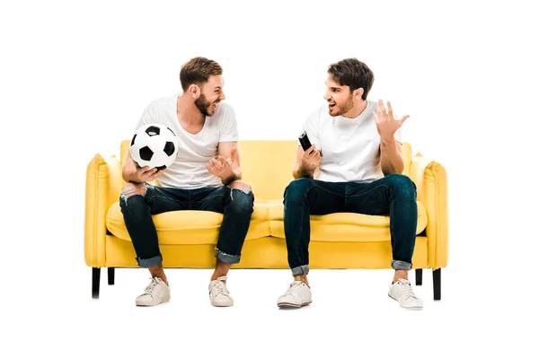 Glückliche junge Männer mit Fußball und Fernbedienung, die sich vereinzelt auf weiß anschauen — Stockfoto