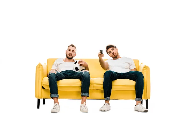 Нудні чоловіки з футбольним м'ячем і пультом дистанційного керування сидять на дивані і дивитися телевізор ізольовано на білому — стокове фото