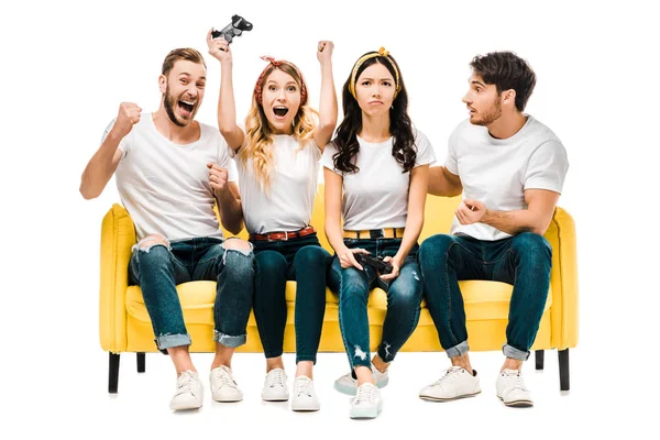 Jóvenes amigos emocionales sentados en el sofá y jugando con joysticks aislados en blanco - foto de stock