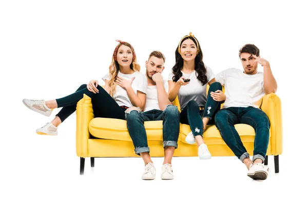 Aburridos hombres jóvenes y mujeres felices sentados en el sofá con mando a distancia y viendo la televisión aislada en blanco — Stock Photo