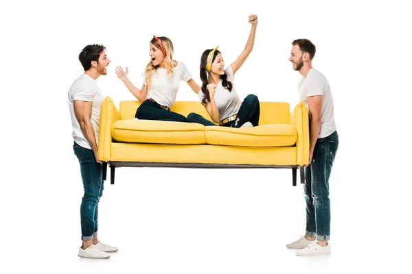 Glückliche junge Männer halten Sofa mit schönen Mädchen, die darauf sitzen isoliert auf weiß — Stockfoto