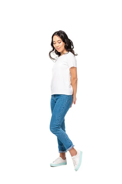 Confused asian woman in white t-shirt and blue jeans holding hands behind back isolated on white — Stock Photo