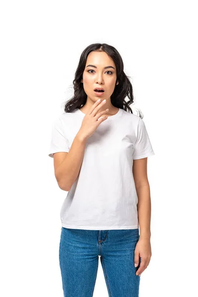 Mujer asiática estresada en camiseta blanca y jeans azules sosteniendo la mano cerca de la cara aislada en blanco — Stock Photo