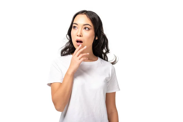 Mujer asiática ansiosa en camiseta blanca sosteniendo la mano cerca de la cara aislada en blanco - foto de stock