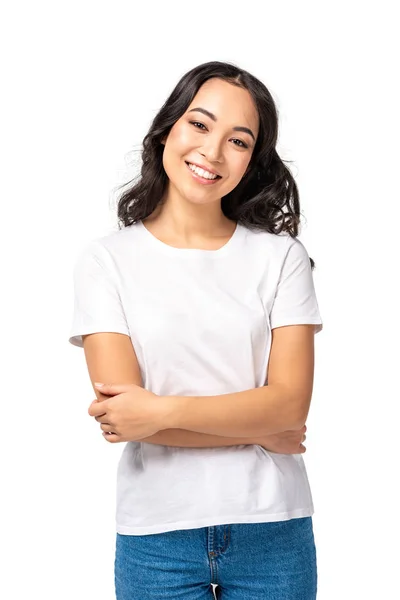 Улыбающаяся азиатская молодая женщина в белой футболке стоящая со скрещенными руками изолированная на белом — стоковое фото