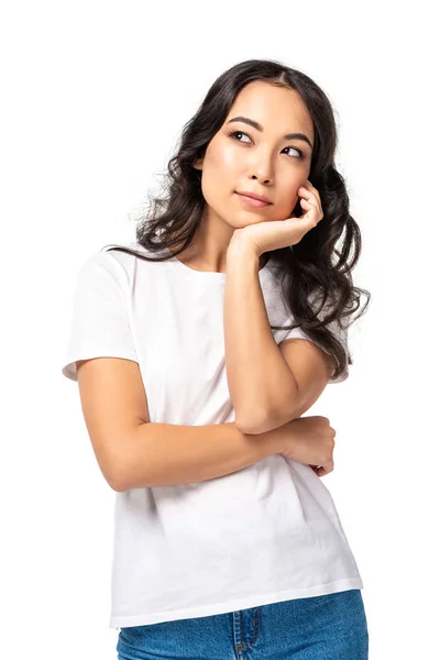 Pensive young asian woman in white t-shirt holding hand under chin isolated on white — Stock Photo