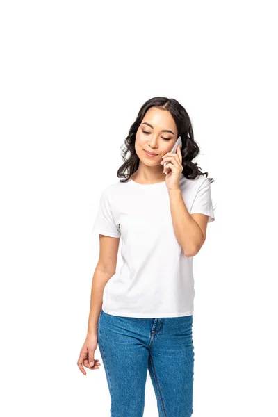 Pretty sian girl with closed eyes in white t-shirt and blue jeans talking on smartphone isolated on white — Stock Photo