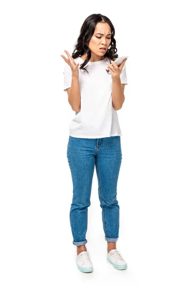 Angry asian girl in white t-shirt and blue jeans using smartphone isolated on white — Stock Photo