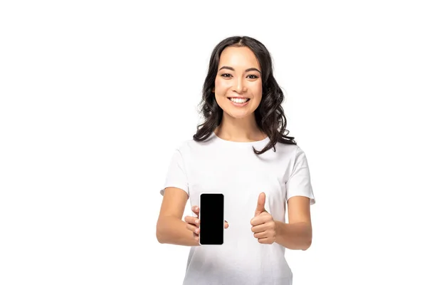 Sonriendo chica asiática sosteniendo teléfono inteligente con pantalla en blanco y mostrando el pulgar hacia arriba aislado en blanco - foto de stock