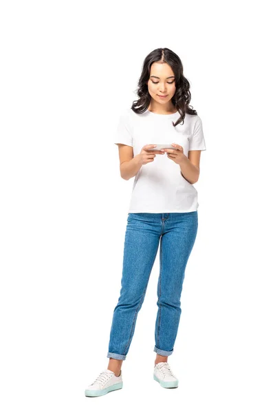 Mujer asiática sonriente en camiseta blanca y jeans azules usando smartphone aislado en blanco - foto de stock