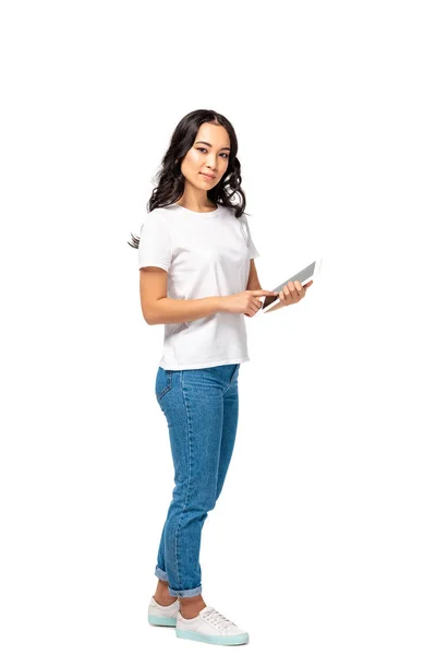 Досить азіатська жінка в білій футболці і синіх джинсах, використовуючи цифровий планшет, дивлячись на камеру ізольовано на білому — стокове фото