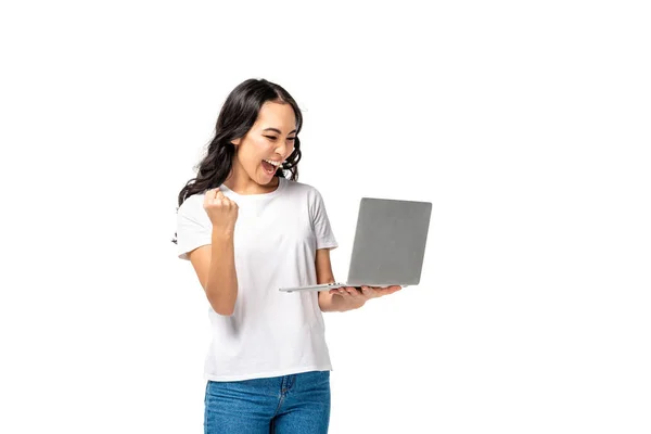 Glückliche junge Asiatin in weißem T-Shirt und blauer Jeans mit Laptop und erhobener Faust isoliert auf weißem Hintergrund — Stockfoto