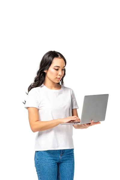 Серйозна молода відеочат жінка в білій футболці і синіх джинсах, використовуючи ноутбук ізольовано на білому — стокове фото