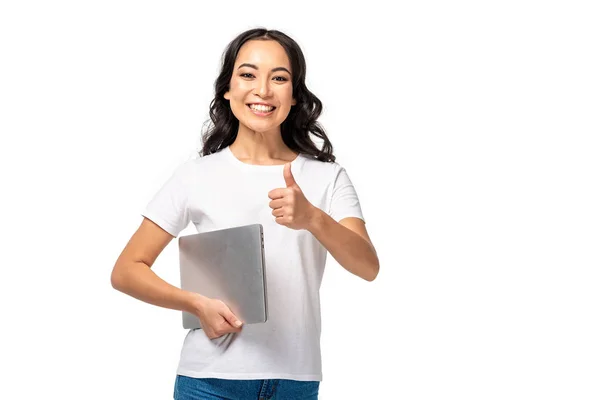 Sorridente donna asiatica in t-shirt bianca e jeans blu tenendo il computer portatile e mostrando pollice in su isolato su bianco — Foto stock