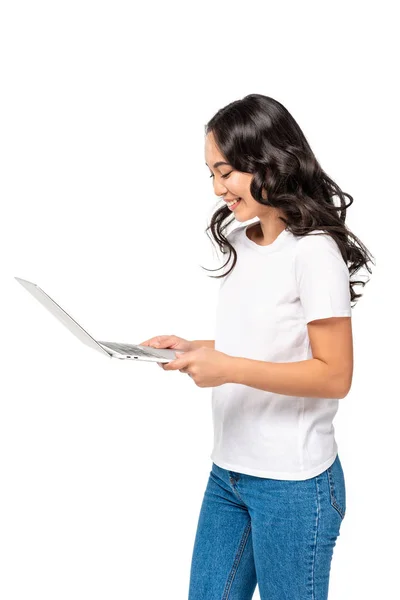 Усміхнена красива азіатська жінка в білій футболці і синіх джинсах, використовуючи ноутбук ізольовано на білому — Stock Photo