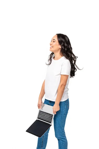 Щаслива азіатська жінка в білій футболці і синіх джинсах тримає ноутбук вниз і сміється ізольовано на білому — стокове фото
