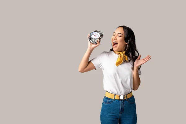 Smiling asian woman holding alarm clock in raised hand isolated on grey — Stock Photo