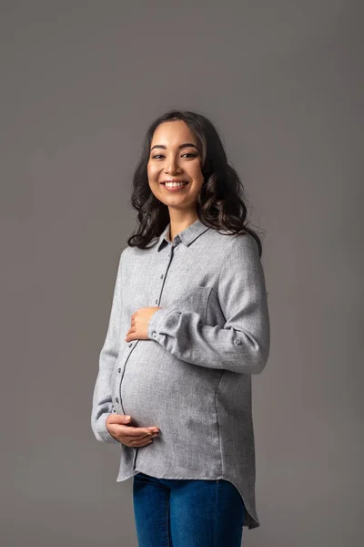 Sorrindo jovem grávida asiático mulher segurando barriga com as mãos isoladas no cinza — Fotografia de Stock