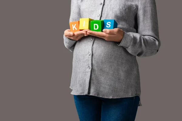 Cropped view of pregnant asian woman holding alphabet cubes with word kids isolated on grey — Stock Photo
