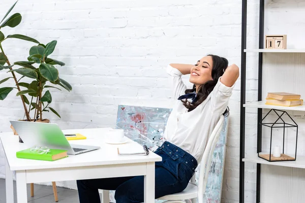 Lächelnde asiatische Freiberuflerin lehnt sich auf Stuhl zurück, die Hände hinter dem Kopf verschränkt — Stockfoto