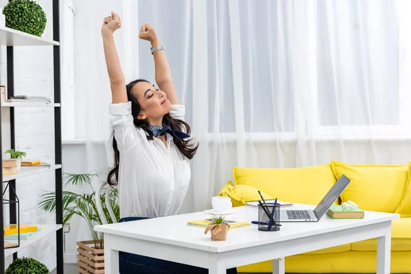 Müder asiatischer Freiberufler streckt sich mit erhobenen Händen auf Stuhl, während er zu Hause am Schreibtisch sitzt — Stockfoto