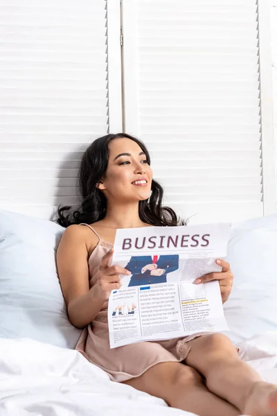 Young asian woman reading business newspaper while staying in bed — Stock Photo