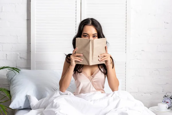 Beautiful asian woman in elegant nighty with obscured face sitting in bed — Stock Photo