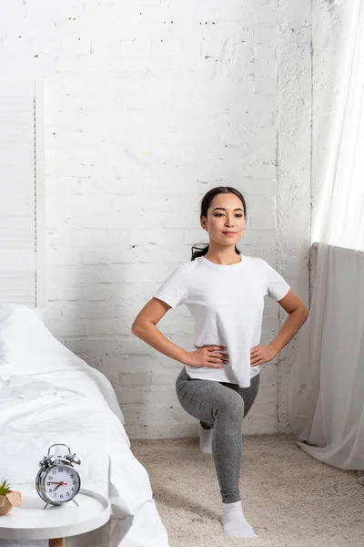 Asian woman in white t-shirt and grey leggings doing lunges exercises — Stock Photo