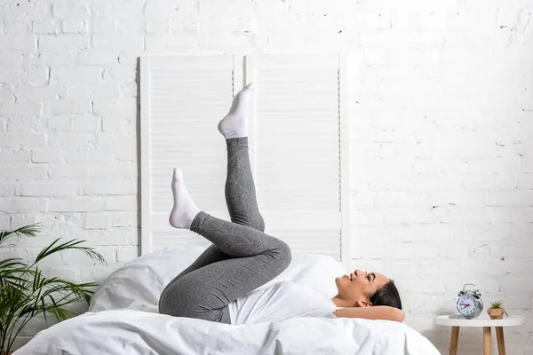 Mujer asiática en camiseta blanca y leggins grises haciendo ejercicios en la cama - foto de stock