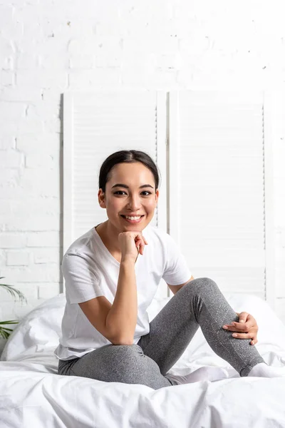 Feliz joven asiática mujer sentada en la cama y descansando después de la mañana ejercitando - foto de stock