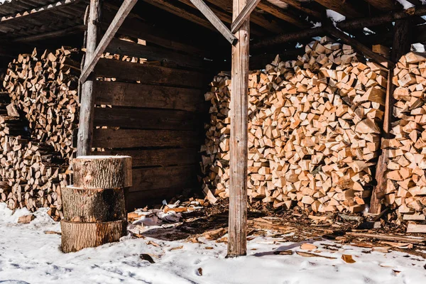 Pile de bois de chauffage dans le bâtiment en bois à la journée ensoleillée en hiver — Photo de stock