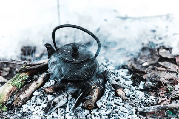 Boiling kettle with steam on firewood and ash in winter forest — Stock Photo