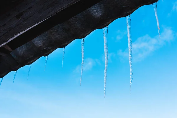 Scharfe Eiszapfen auf dem Dach gegen strahlend blauen Himmel — Stockfoto