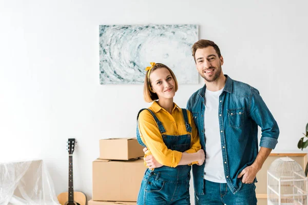 Smiling couple in jeans standing near cardboard boxes at home — Stock Photo