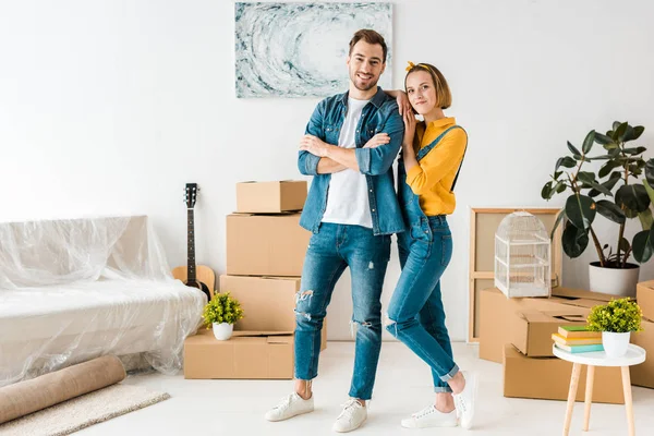 Полный вид счастливой пары, стоящей рядом с картонными коробками дома — стоковое фото