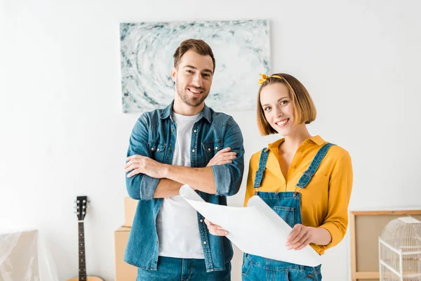 Joyeux couple souriant en jeans avec un plan à la maison — Photo de stock