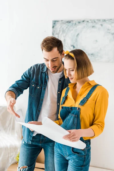 Fröhliches Paar in Jeans schaut sich Bauplan zu Hause an — Stockfoto