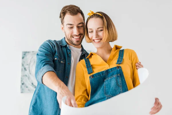 Laughing couple in jeans looking at blueprint at home — Stock Photo
