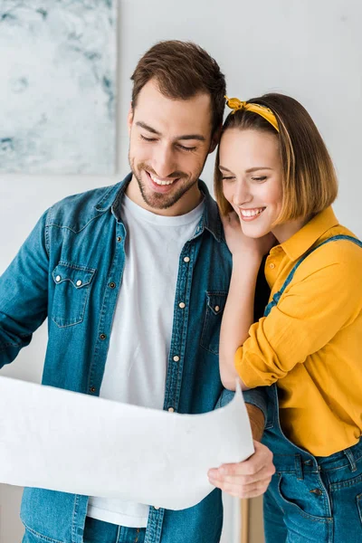 Fröhliches Paar in Jeans schaut sich Bauplan zu Hause an — Stockfoto