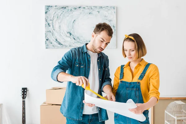 Konzentriertes Paar mit Maßband und Blaupause zu Hause — Stockfoto