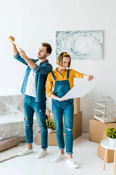 Full length view of focused couple with measuring tape and blueprint — Stock Photo