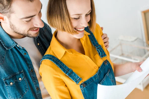 Cropped view of laughing couple looking at blueprint — Stock Photo