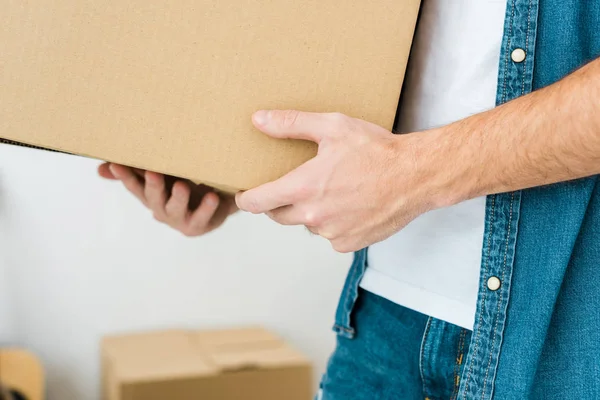 Partial view of man in denim shirt holding cardboard box — Stock Photo