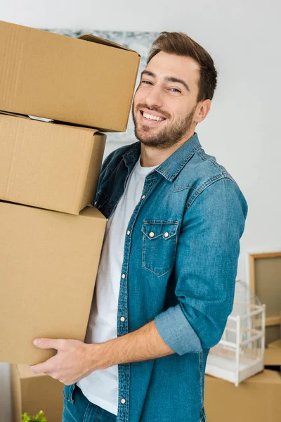 Joyful man in denim jacket holding cardboard boxes and looking at camera — Stock Photo