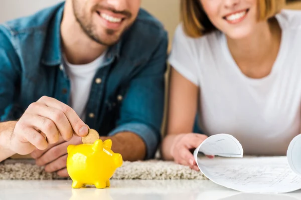 Vue recadrée du couple souriant avec plan et tirelire couché sur le tapis — Photo de stock