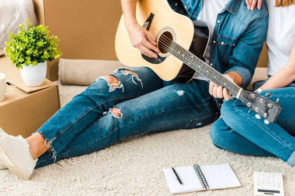 Вид человека, сидящего на ковре с женой и играющего на акустической гитаре — стоковое фото